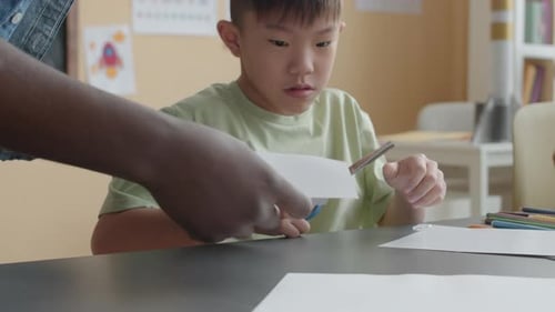 Teacher Helping Student Cut Paper in Classroom