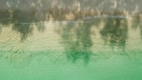 Bird's eye view of ocean waves crashing against an empty sand beach from above.