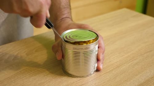 Opening Can of Corn with Knife on Table
