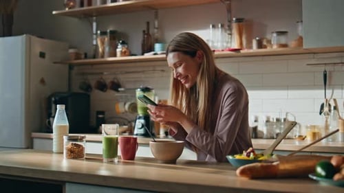 Woman Enjoying Breakfast and Mobile Phone in Kitchen
