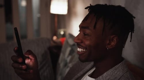 Young black male wears a big smile while looking at his smart phone