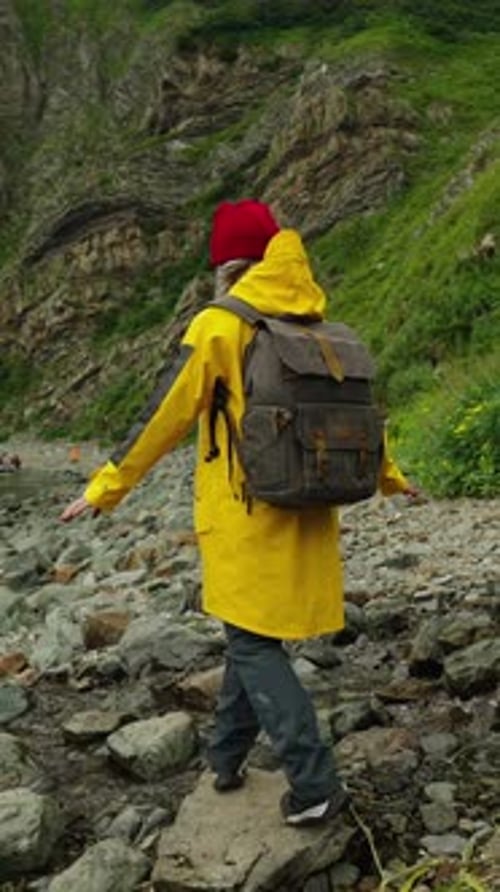 Exploring Nature's Beauty A Hiker in a Bright Yellow Raincoat and Backpack Walking Along a Rocky