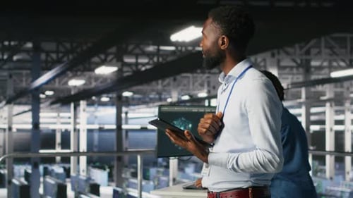 Technician Walks in Data Center Doing Maintenance Tasks on Tablet