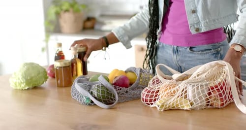 Joven afroamericana desempacando alimentos en la cocina, en casa, espacio para copiar
