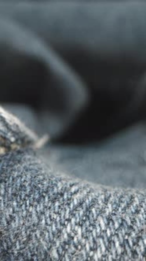 Vertical video. The texture of blue denim fabric and a metallic zipper. Dolly slider macro