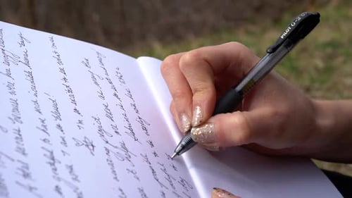 Woman's hand with beautiful manicure writing on a notepad - close up