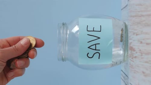 Hand Deposits Coins in Saving Jar