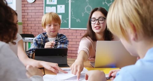 Young Female Teacher Sitting at Desk Together with Little Teens Clever Pupils Woman Teaching