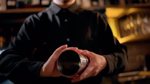 Closeup of a Bartender in a Dim Bar Assembling Stainless Steel Cocktail Shakers Preparing to Mix a