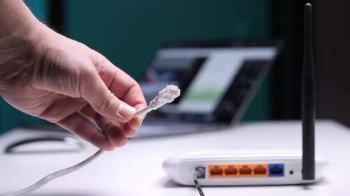 Hand holding ethernet cable next to wireless router