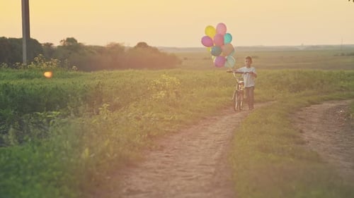 Boy Walks with Balloons and Bicycle at Sunset