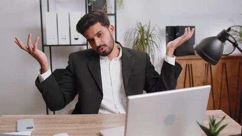 Confused Man Shrugs Shoulders at Office Desk