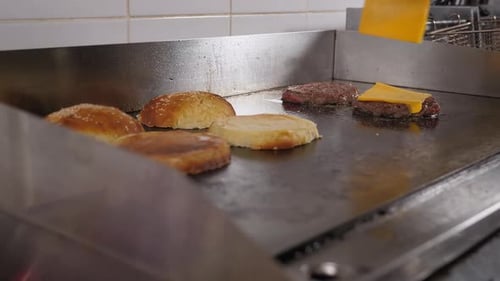 The Chef Puts Cheese on Burger Patties on the Stove in the Restaurant Kitchen