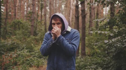 Jeune homme gelé serrant les mains dans les poings se réchauffant les mains avec son souffle debout dans la forêt