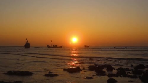 Silhouette of Fishing Boats floating on the calm blue ocean with the orange sunset in the background