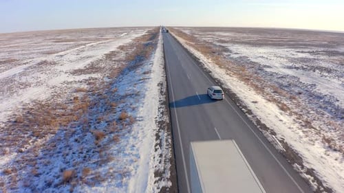 A view from the back of a silver car passing by oncoming trucks