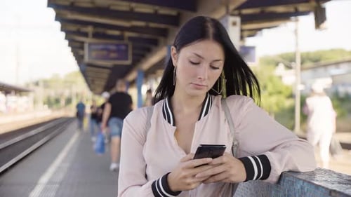 Eine junge schöne kaukasische Frau arbeitet an einem Bahnhof auf einem Smartphone