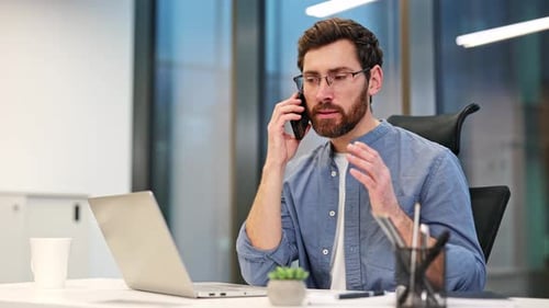 Businessman Talking on Phone and Working on Laptop in Office