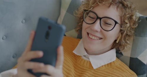 Smiling Woman Using Smartphone While Lying on Couch