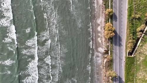Top down aerial footage of long waves on a beach next to the road