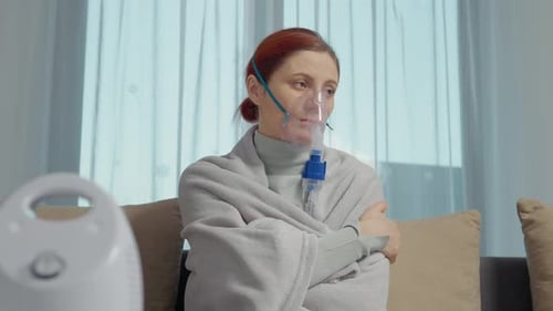 Une femme est assise à la maison et utilise un nébuliseur pour la thérapie par inhalation