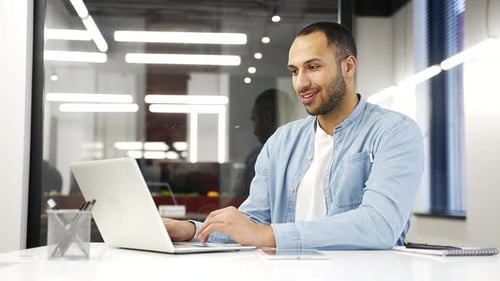 Young african american businessman working on laptop in modern office, smiling while typing. Black