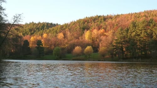 A serene lake reflects the vibrant autumn colors of a forested hillside.