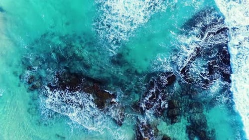 4k aerial drone shot of beautiful tropical blue ocean with waves breaking on rocks