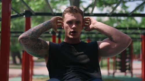 young muscular sportsman bodybuilder doing abs exercises during street workout on sports ground