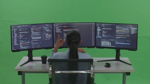 Back View Of Asian Woman Developer Thinking While Write Code With Multiple Screens In Green Screen