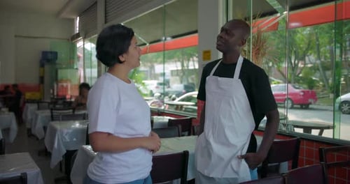 African American waiter listening to female manager during conversation in restaurant, standing