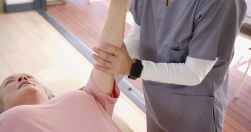 Caregiver Stretching Senior's Arm During Physical Therapy Session