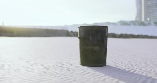 Black Trash Can Sits Alone on Sandy Beach at Sunrise