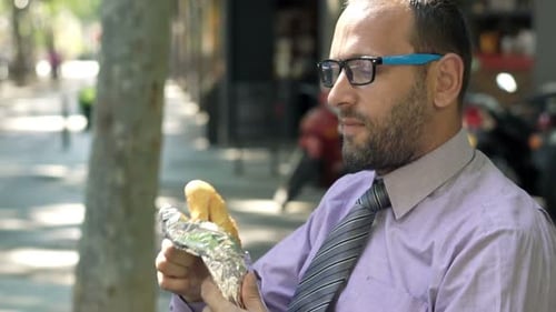 Young Businessman Eating Sandwich on Bench in City 30s