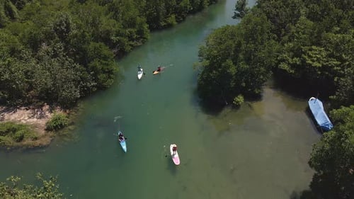 Aerial drown birds eye view slow moving backwards dolly of paddle boarders slowly paddling up river