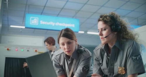 Airport Security Checkpoint Female TSA Officer Wearing Headset Uses Laptop Talks to Colleague