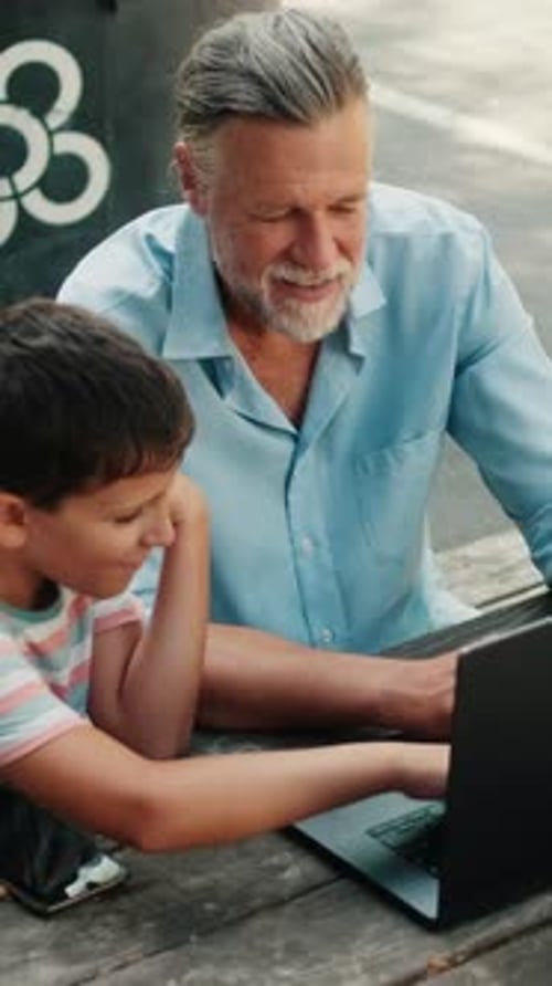 Vertical video, Grandfather and Grandson Use Laptop at Park