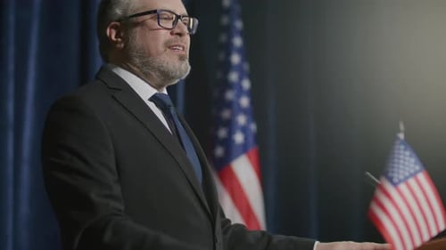 Man Giving Speech at Podium with USA Flags