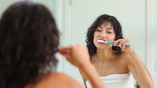 Woman Brushing Teeth in Bathroom Mirror