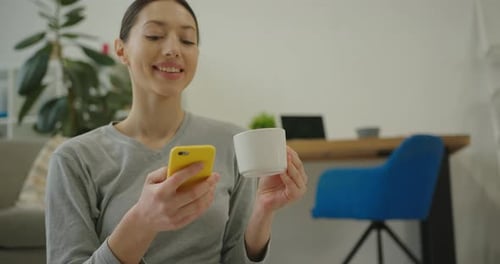 Woman Uses Phone, Drinks from Cup Indoors