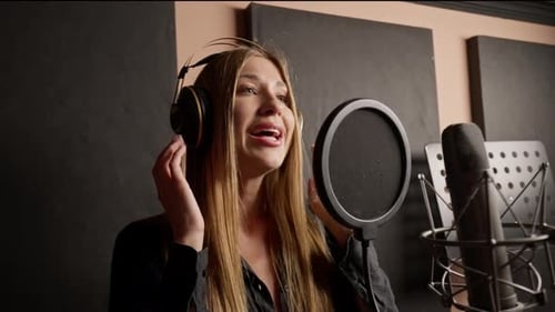 girl singer singing in a recording studio with headphones in front of microphone to create a song