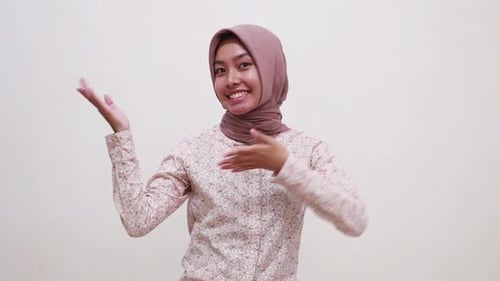 Carefree young asian muslim girl standing while presenting both sides and showing thumbs up. Isolate
