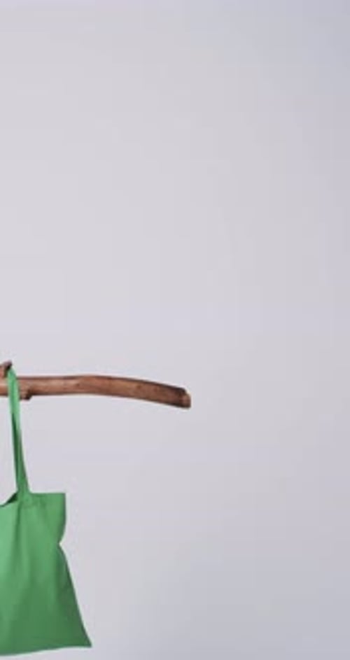 Vídeo vertical de una bolsa de lona verde que cuelga de una rama con espacio para copiar sobre fondo blanco