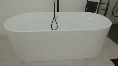 Freistehende weiße Badewanne mit schwarzem Brauseschlauch