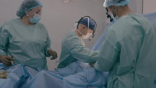 Surgeon with Assisting Man Doctor Operating Patient Perform Surgical Procedure Nurse Woman Stand at