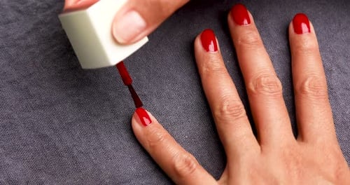 Woman Applying Red Nail Polish to Finger