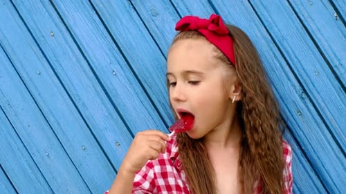 Girl Enjoys Lollipop in Front of Blue Wall