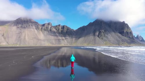 Aerial slow motion view of woman jogging on Atlantic ocean coast. Sea waves washing black sandy beac