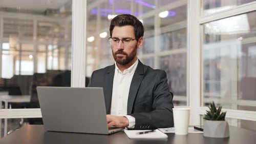 Businessman Takes Off Glasses After Working on Laptop at Desk in Office