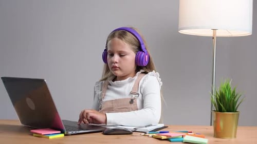 Homeschooling Online School Girl in a Purple Headphones Sitting at the Table at Home and Uses a